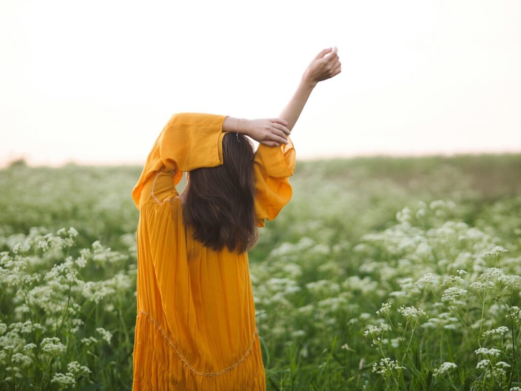 A woman in an orange dress with arms stretched, enjoying a field of wildflowers.